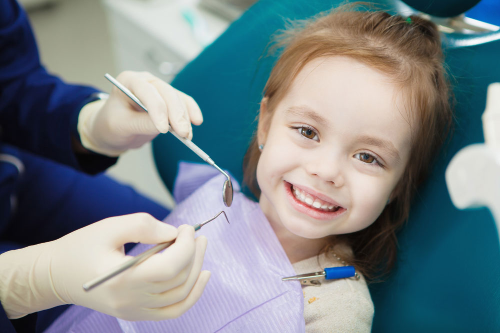Child with cute smile sits at dentist chair with napkin