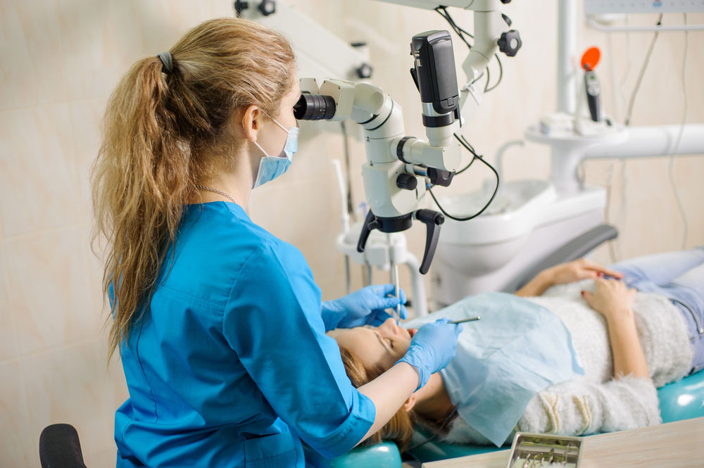Young female dentist treating root canals using microscope at the dental clinic
